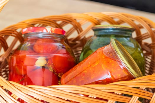 Jars with different types of pickles and preserves in a wicker basket. Food