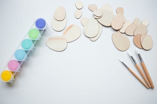 Wooden Easter egg shapes with paint and brushes with copy space for creative crafting.