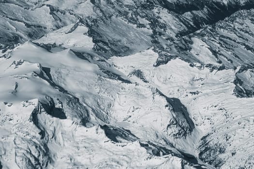 Aerial view of high rocky mountains covered with snow. Alpine landscape. Beauty in nature. Inaccessible mountain peaks. Harsh climate. Looking at the Earth from an airplane window. Aerial view of the land
