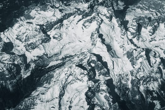 Aerial view of high rocky mountains covered with snow. Alpine landscape. Beauty in nature. Inaccessible mountain peaks. Harsh climate. Looking at the Earth from an airplane window. Aerial view of the land