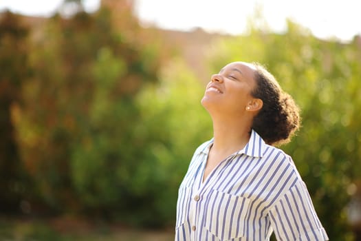 Happy black woman breathing fresh air standing in a park