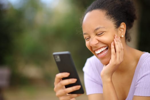 Funny black woman checking phone laughing loud in a park