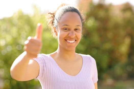 Front view portrait of a happy black woman gesturing thumbs up outdoors