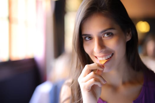 Happy woman in a restaurant eating chips and looking at you