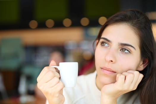 Pensive serious woman holding coffee cup in a bar interior