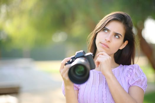 Doubtful photographer thinking what to shoot holding camera in a park