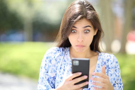 Front view of a perplexed woman checking phone in the street