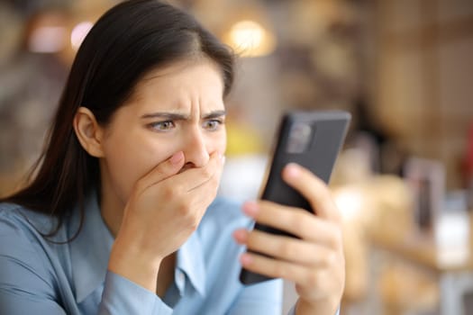 Terrified woman watching media content on phone in a restaurant