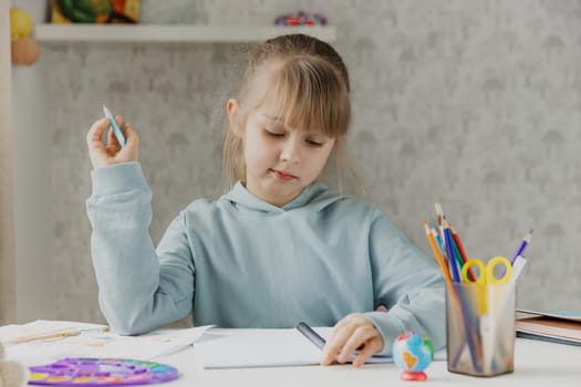 Schooler cute little girl sitting at desk in bedroom, holding a pen, doing homework, kid studying at home, getting ready before exams, writing notes. Home education, homeschooling