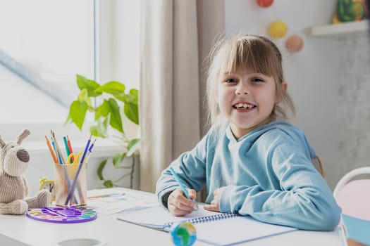 Schooler cute little girl sitting at desk in bedroom, holding pencil, doing homework, kid studying at home, writing notes. Home education, homeschooling. Child smiling, happy because of successul task