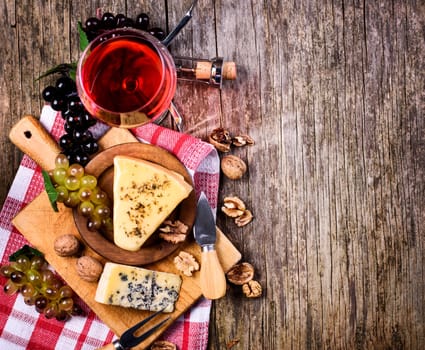Top view of red wine, grape and cheese on rustic wooden table background with copyspace. French cuisine product from above. Wine and dine still life. Top view.