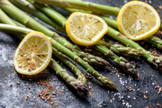Fresh asparagus dish with lemon and spices on black plate closeup. Vegetarian cuisine recipe.