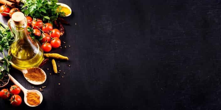 Food background. Top view of olive oil, cherry tomato, herbs and spices on rustic black slate. Colorful food ingredients border. Italian cuisine.