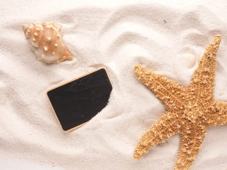 Starfish and shell with small chalkboard in sandy beach, vacation concept, tropical beach