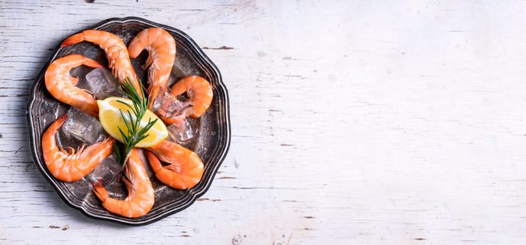 Top view of seafood platter with herbs and spices on white wooden table. Food background with copyspace. Shrimps in vintage plate with lemon from above. Fresh prawns salad dish cooking. Overhead.