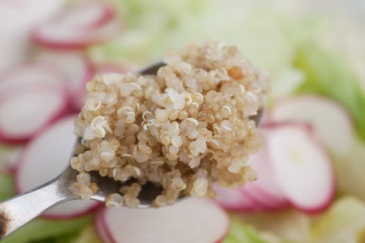 Healthy quinoa sits on a spoon, surrounded by fresh vegetables.