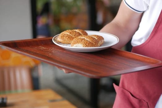A waiter presents a plate of sesame buns on a wooden tray at a cafe.