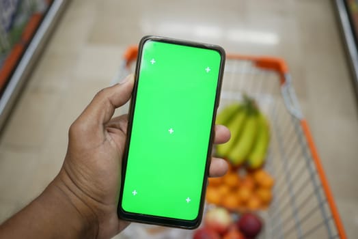 A hand is holding a smartphone displaying a green screen while shopping.