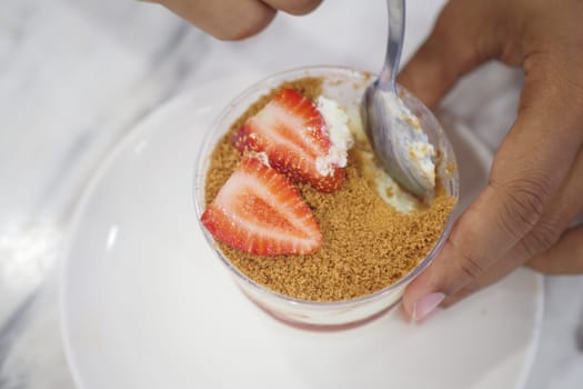 A hand holds a spoon ready to enjoy a dessert with strawberries.