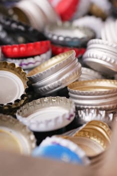 Various bottle caps are spilled together in a cardboard box.