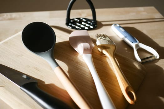 A variety of kitchen tools laid out on a cutting board during the day.