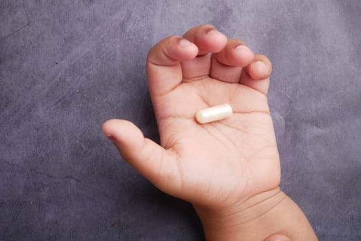 A small hand is holding a single dietary supplement capsule, showcasing care.