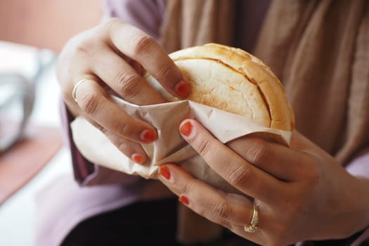 A person unwraps a sandwich while seated at a cozy cafe.