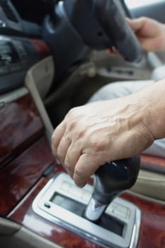 A hand changes gears while driving in a car during the day.