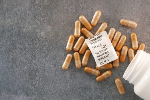 Gel capsules and silica packets are strewn across a gray surface.