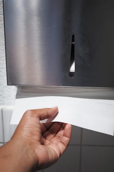 Individual pulls a paper towel from a wall-mounted dispenser.