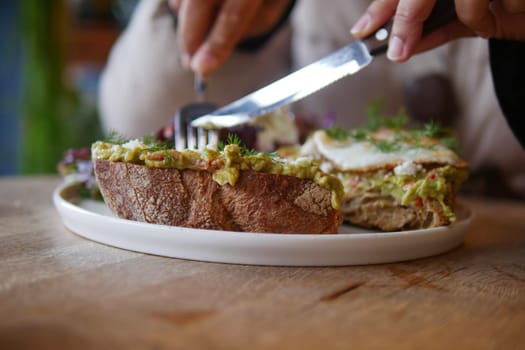 A person is cutting a fresh open-faced sandwich topped with avocados.