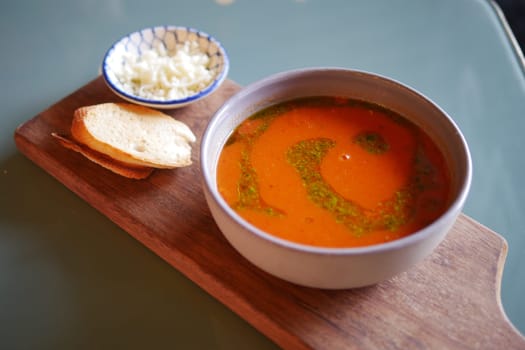 Warm tomato soup accompanied by sliced bread and cheese on the side.