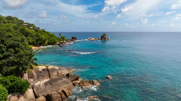 Clear turquoise water with waves hitting rocky shoreline and greenery in the background. Seychelles, Mahe.