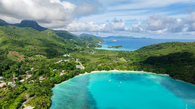 Mountainous coastline with beach and a turquoise bay, boats floating in the bay. Seychelles, Mahe. Launay Beach.