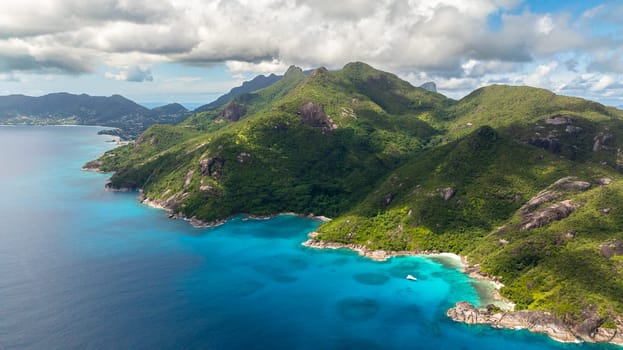 Turquoise waters stretching along the green mountain slopes with clear skies above. Seychelles, Mahe.