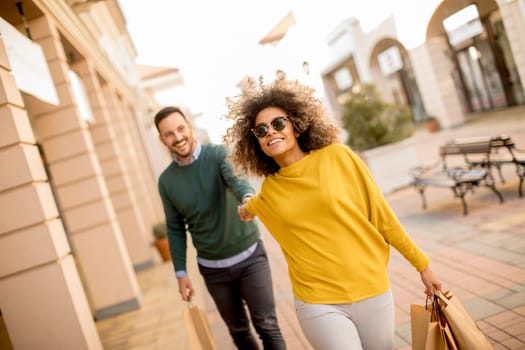 Young and cheerfull couple walking along street with shopping bags