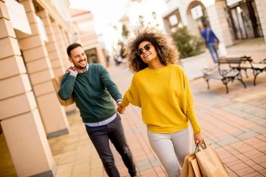 Young and cheerfull couple walking along street with shopping bags