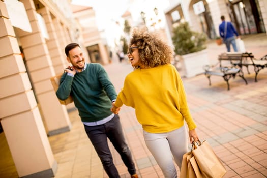 Young and cheerfull couple walking along street with shopping bags
