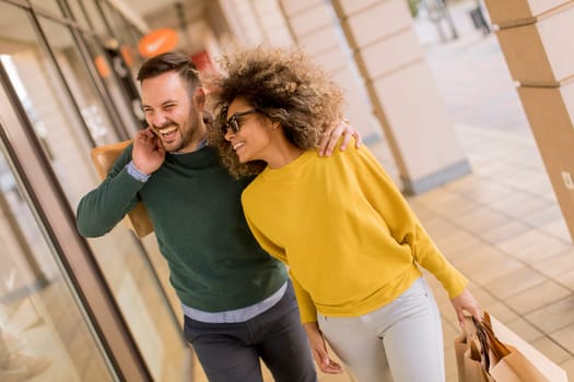 Beautiful young multiethnic couple with paper bags enjoying in shopping, having fun in the city