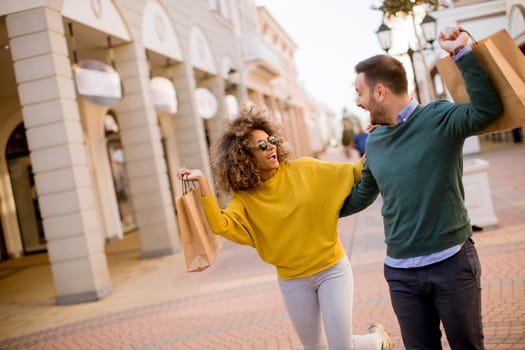 Beautiful young multiethnic couple with paper bags enjoying in shopping and having fun in the city