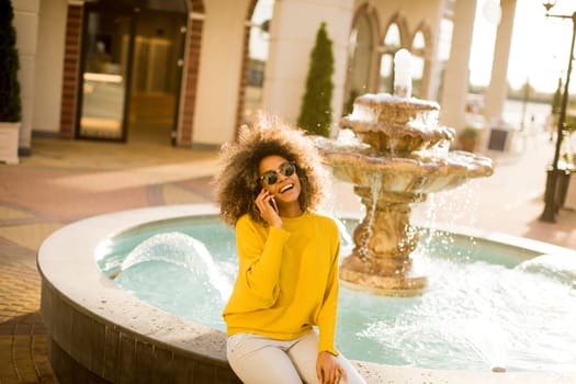 Attractive young woman with curly hair using her touch screen mobile cell phone by the fountain