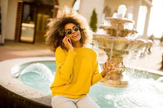 Attractive young woman with curly hair using her touch screen mobile cell phone by the fountain