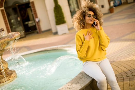 Aftican american young woman sits near fountain and talks on smartphone