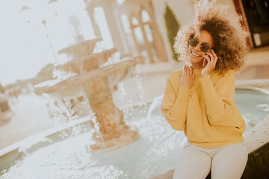 Aftican american young woman sits near fountain and talks on smartphone