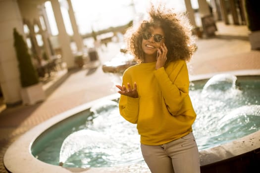 Attractive young woman with curly hair using her touch screen mobile cell phone by the fountain
