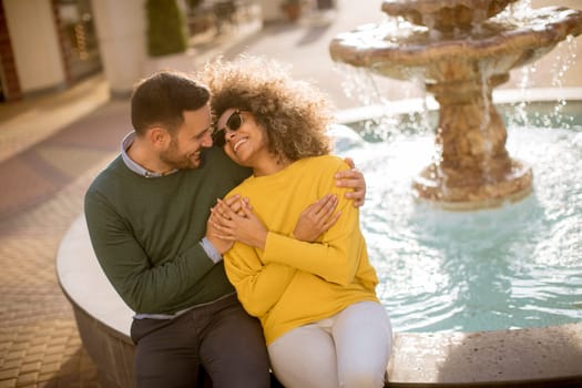 Portrait of beautiful smiling love couple sitting near fountain on a sunny day