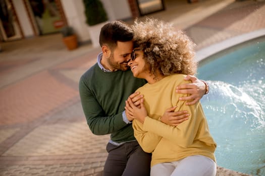 Portrait of beautiful smiling love couple sitting near fountain on a sunny day