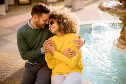 Portrait of beautiful smiling love couple sitting near fountain on a sunny day