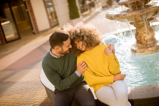 Portrait of beautiful smiling love couple sitting near fountain on a sunny day
