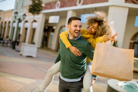 Portrait of  young man holds young woman on his back , have fun and go to shopping